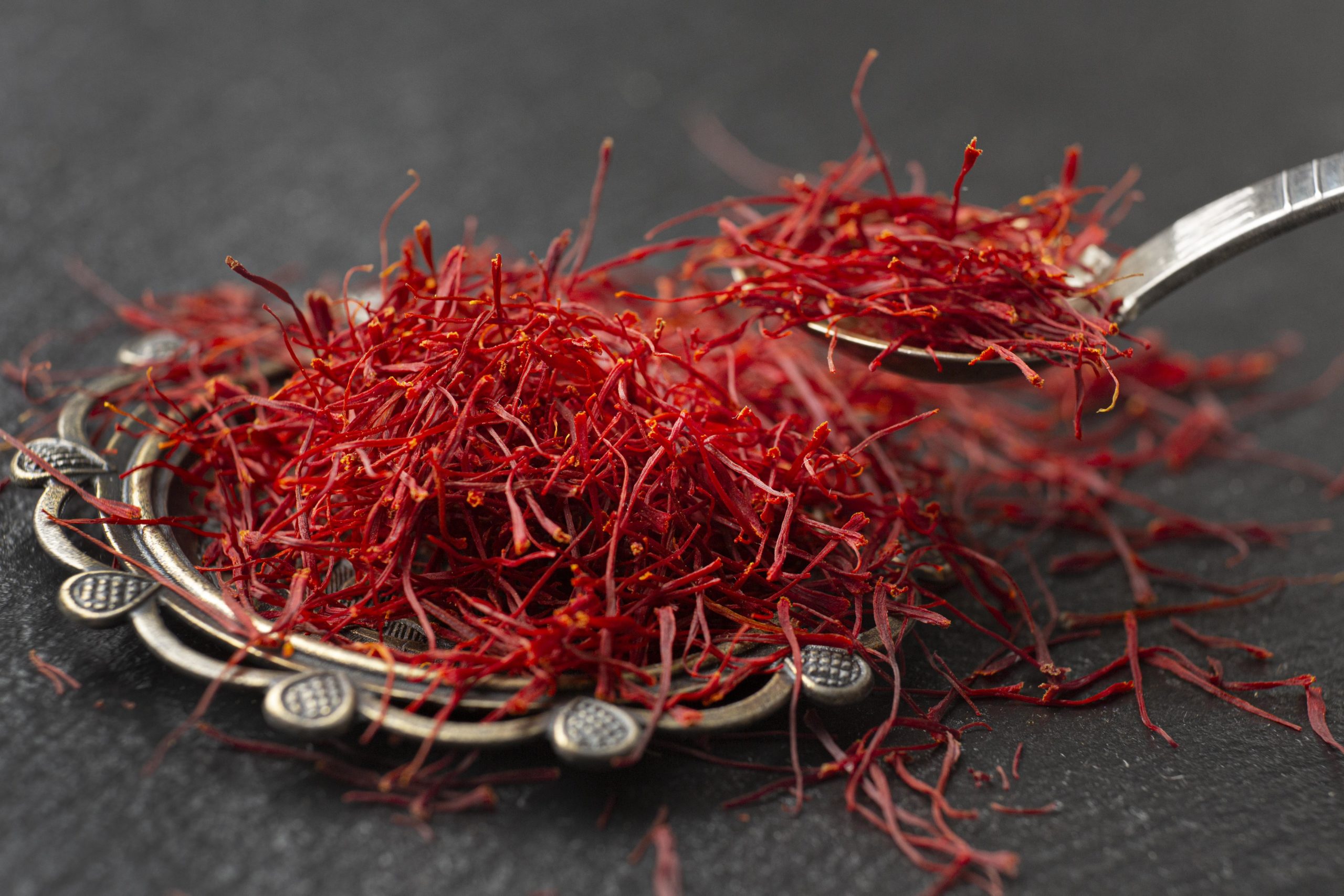 Photo of a silver plate overflowing with red saffron threads and a spoonful of saffron being scooped up.